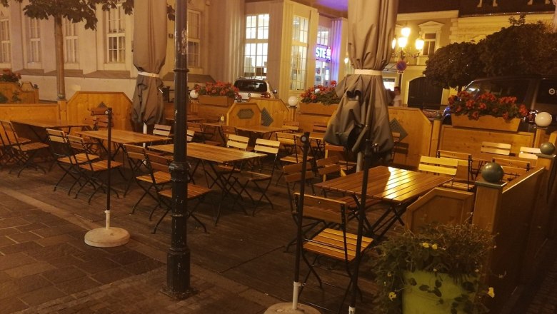 Adlerbräu Außenbereich, © Roman Zöchlinger Außenbereich eines Restaurants mit leeren Holztischen und Stühlen, umgeben von Pflanzen und Laternen bei Nacht.