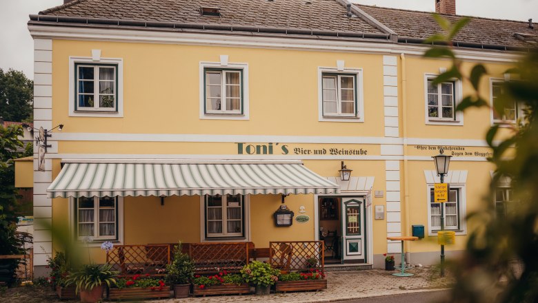Wirtshaus mit Geschichte in Kilb, © Niederösterreich Werbung/Daniela Führer Gelbes Gebäude mit Markise und Pflanzen, beschriftet mit 'Toni's Bier- und Weinstube'.