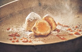 Eismarillenknödel, © Niederösterreich Werbung/Andreas Hofer Eismarillenknödel mit Puderzucker und Aprikosensauce auf einem Sieb.