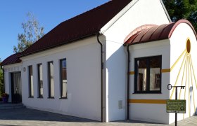 Amethystkapelle Grübern, © Stadtgemeinde Maissau Weiße Kapelle mit rotem Dach und gelben Akzenten, umgeben von gepflastertem Boden und Pflanzen.