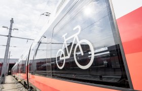 Zug, © Weinviertel Tourismus GmbH / Herbst Nahaufnahme eines roten Zuges mit einem Fahrradsymbol auf dem Fenster.