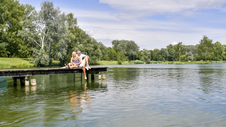 Aubad und Erholungspark Tulln, © Stadtgemeinde Tulln/Robert Herbst Ein Paar sitzt auf einem Steg am Wasser im Aubad und Erholungspark Tulln.