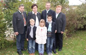 Fam. Pöhn, © Landgasthof Pöhn Eine Familie steht draußen in einem Garten, alle tragen formelle Kleidung. Im Hintergrund sind Büsche und Bäume zu sehen.