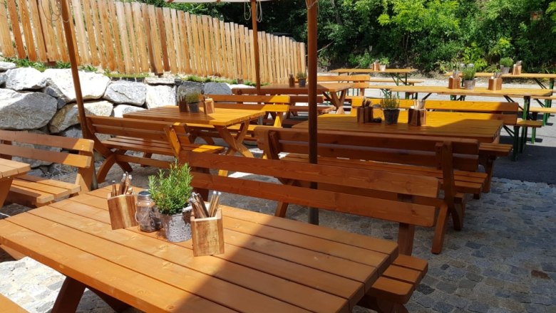 pfefferschiff_garten, © Iris und Jürgen Vigne Holzbänke und Tische im Freien mit Sonnenschirmen und Pflanzen.