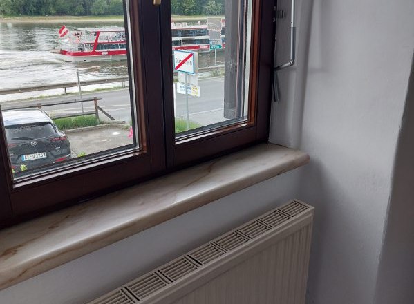 Gästezimmer Weixelbaum, © Familie Weixelbaum Blick aus einem Fenster auf einen Fluss mit einem vorbeifahrenden Boot und einem geparkten Auto.