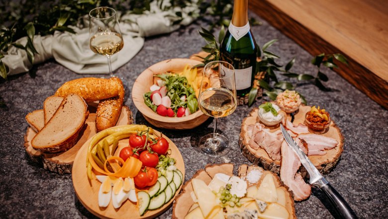 Heurigenjause, © Claudia Müllner Verschiedene Speisen auf Holztellern mit Weinflasche und Gläsern.