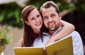 Familie Burger, © Marek Knopp Ein lächelndes Paar hält eine Menükarte beim Heurigen Burger.