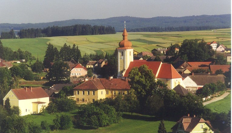 Gemeinde Waldkirchen a. d. Thaya, © Gemeinde Waldkirchen a. d. Thaya Luftaufnahme von Waldkirchen an der Thaya mit Kirche und umliegenden Häusern, umgeben von Feldern und Wäldern.
