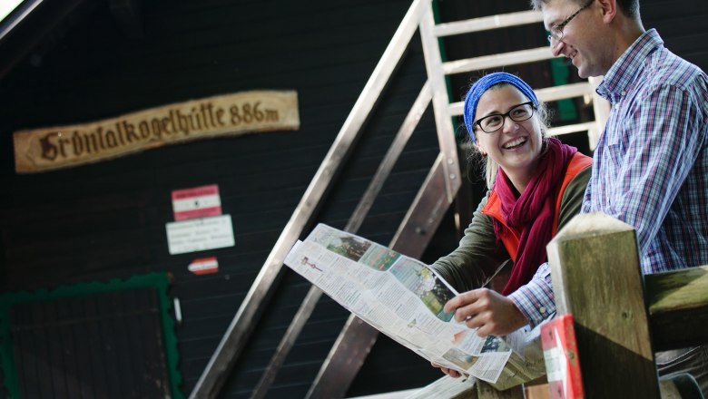 Grüntalkogelhütte, © Doris Schwarz König Zwei Personen sitzen vor der Grüntalkogelhütte und schauen auf eine Karte.