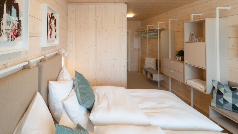Doppelzimmer mit Holzbau, © freilich / IsaBella Fritsche Modernes Doppelzimmer mit Holzwänden, Bett, Kissen und minimalistischer Einrichtung.