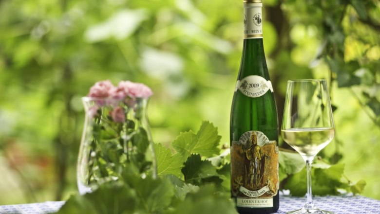 Wein vom Loibnerhof, © Rita Newman Weinflasche und Glas auf Tisch mit Blumen und Blättern im Hintergrund.