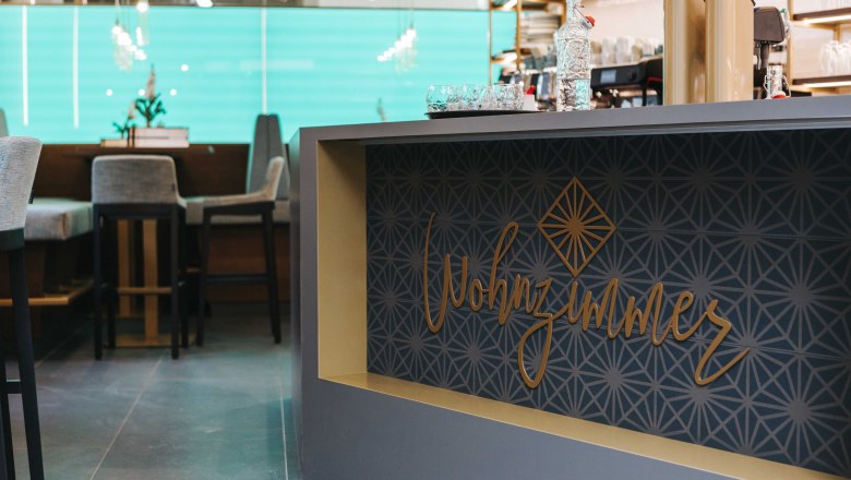 Café Wohnzimmer Logo, © FMS Steinertor Gastronomie BetriebsgmbH Innenansicht eines Cafés mit dem Schriftzug 'Wohnzimmer' auf einer Theke.