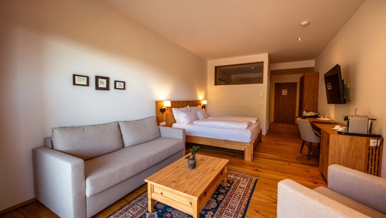 Weinhotel Nigl, © Niederösterreich Werbung / Maximilian Pawlikowsky Hotelzimmer mit Doppelbett, Sofa, Holztisch und Schreibtisch.