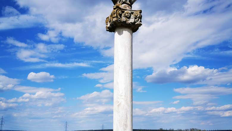 Rustenberg, © Weinstraße Weinviertel Eine Statue auf einer Säule in einer ländlichen Landschaft unter blauem Himmel mit Wolken.