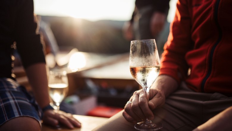 Ahoi Wachau mit Weinglas, © Michael Reichl Person hält ein Weinglas in der Hand, im Hintergrund Sonnenuntergang.