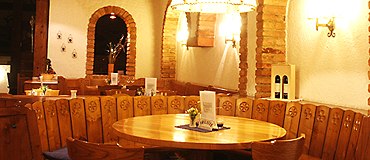 Stüberl, © Weingut Drimmel Urbanuskeller Gemütliches Stüberl mit Holztisch und Stühlen, umgeben von rustikalen Backsteinbögen und warmem Licht.