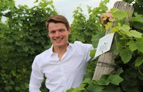 Roman Josef Pfaffl, © Weingut R&A Pfaffl Ein Mann in einem Weinberg neben einem Schild mit der Aufschrift 'Weingut Pfaffl'.