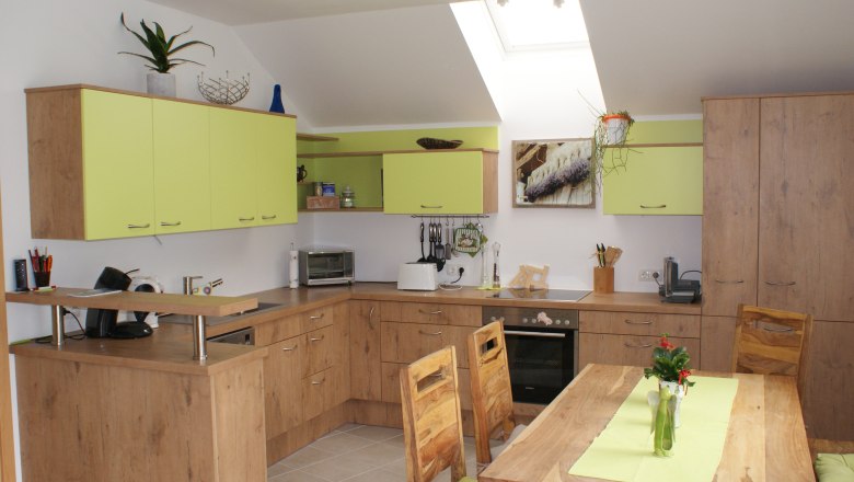 Küche, © Familie Zwinz Moderne Küche mit Holzmöbeln und grünen Akzenten, Esstisch mit Vase, Oberlichter.