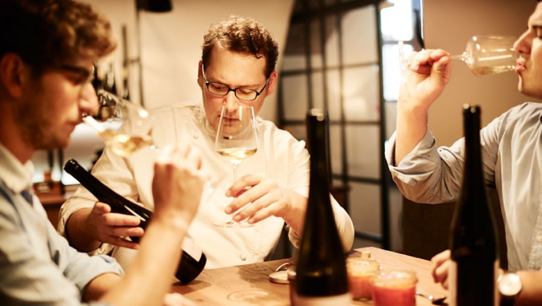 Auf der Weinkarte mit 2.500 Positionen steht auch die Weinhofmeisterei Mathias Hirtzberger, © Michael Winkelmann Drei Männer verkosten Wein an einem Tisch mit Weinflaschen.