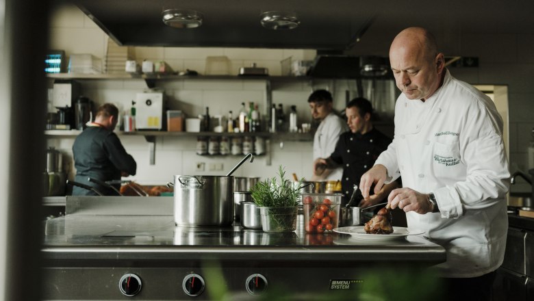 Manfred Hausgnost in der Küche, © Niederösterreich Werbung/Michael Reidinger Köche arbeiten in einer professionellen Küche, einer schneidet Fleisch.