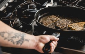 Beliebt: Trilogie vom Waldviertler Karpfen, © Niederösterreich Werbung/David Schreiber Person brät Fischstücke in einer Pfanne auf einem Herd.