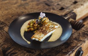 Gehobene, traditionelle Küche von höchster Qualität, © Niederösterreich Werbung/David Schreiber Gebratener Fisch mit Gemüsewürfeln und Sauce auf schwarzem Teller serviert.