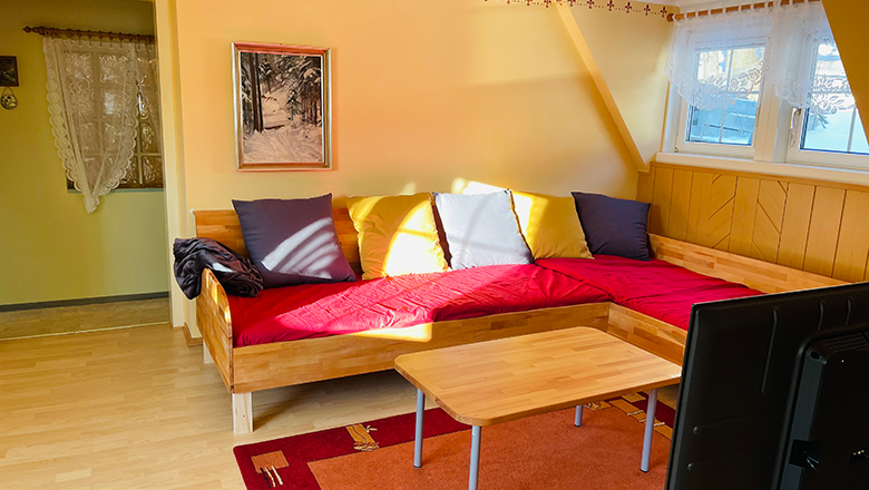 Wohnzimmer, © Angelika Burger Wohnzimmer mit rotem Sofa, Holztisch und Fernseher.