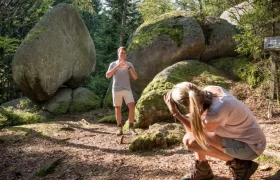 Herzstein, © Matthias Schickhofer Ein Mann posiert vor einem großen herzförmigen Felsen im Wald, während eine Frau ein Foto von ihm macht.
