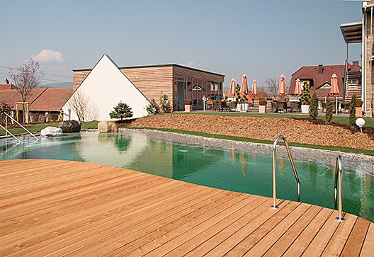 Steg mit Swimmingpool, © Weinresidenz Sonnleitner Ein Holzsteg führt zu einem Swimmingpool, umgeben von Gebäuden und Sonnenschirmen.
