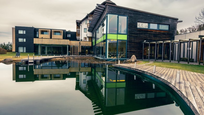 schwarzalm wellness, © Schwarz Alm Modernes Wellnesshotel mit Holzfassade und großem Teich im Vordergrund.