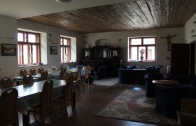 SOLA Safov, © Hannes Messmann Ein gemütlicher Raum mit Holztischen, Stühlen und Sofas, dekoriert mit Teppichen und Bildern an den Wänden.