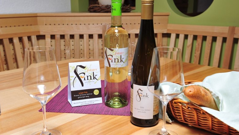 Weine Weinhof Fink, © Philipp Monihart Zwei Weinflaschen und Gläser auf einem Holztisch mit Brotkorb.