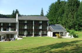 BS Ötscher Hotel im Sommer, © Familie Butt Hotelgebäude mit Solarpanelen und grüner Wiese im Vordergrund, umgeben von Wald.