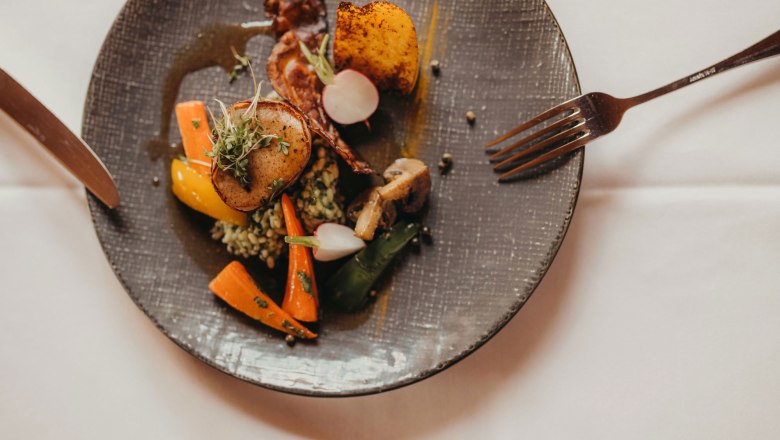 Rosa Schweinsfilet im Bauchspeckmantel mit Bärlauchrisotto, © Niederösterreich Werbung/Daniela Führer Ein Teller mit Schweinsfilet im Speckmantel, Bärlauchrisotto, Gemüse und Kartoffeln.