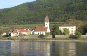 Pfarrkirche Hofarnsdorf, © Robert Schütz Pfarrkirche Hofarnsdorf mit umliegenden Gebäuden und bewaldetem Hügel im Hintergrund, aufgenommen von der Donau aus.