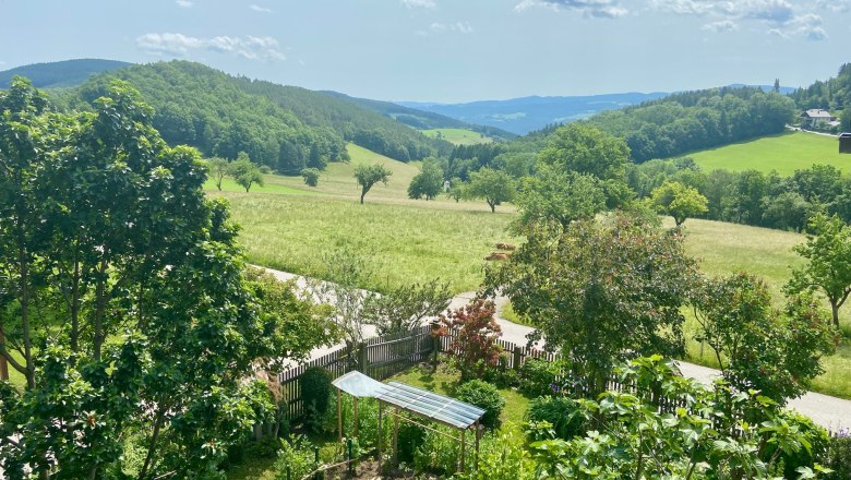 Ferienwohnungen Riedl, © Wiener Alpen Landschaft mit grünen Hügeln, Bäumen und einem kleinen Garten im Vordergrund.