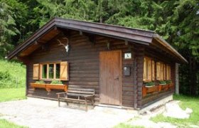 Jagdhaus, © Archiv Ein kleines, rustikales Jagdhaus aus Holz mit Fensterläden und Geweih an der Fassade, umgeben von Wald.