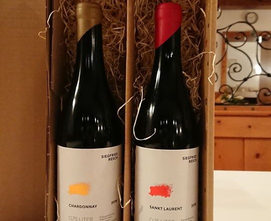 Weingut Siegfried Resch, Flaschendesign, © Siegfried Resch Zwei Weinflaschen in einer Kartonverpackung mit Stroh, im Hintergrund eine Backsteinwand.