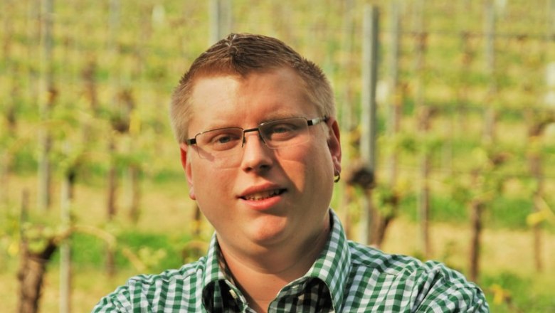 Winzer Martin Schwinner, © Weingut Schwinner Ein Mann mit Brille und kariertem Hemd steht mit verschränkten Armen vor einem Weinberg.