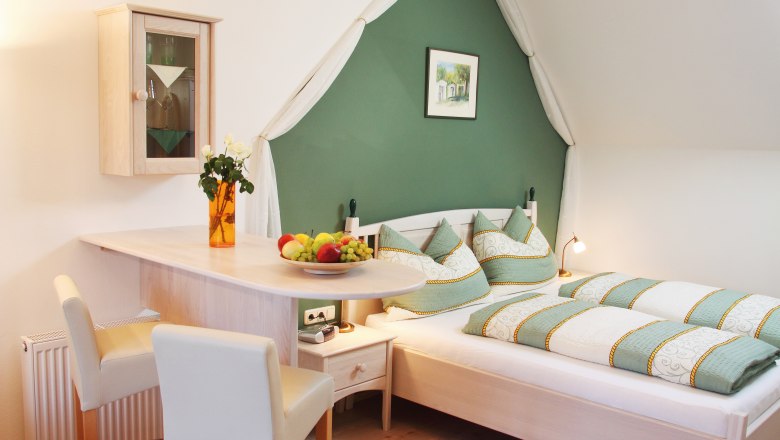 Genießerzimmer „Weinviertel“, © Weingut Stur/Christian Mrozowsky Gemütliches Schlafzimmer mit grün-weißer Bettwäsche, Holzmöbeln und Dekorationen.