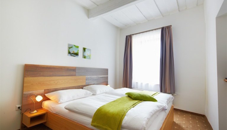 Standard DZ, © Rathauskeller Melk Helles Schlafzimmer mit Doppelbett, grünem Überwurf und zwei kleinen Bildern an der Wand.