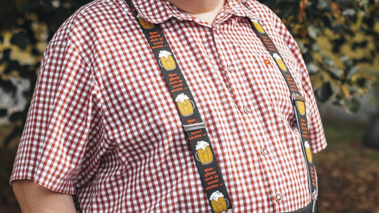 Wirt: Herbert Scheiterer, © Niederösterreich Werbung/David Schreiber Ein Mann in kariertem Hemd und Hosenträgern steht lächelnd vor einem Baum.