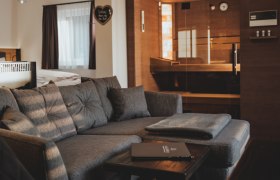 ChaLaaLets, © Fam. Oberrenzer Gemütliches Wohnzimmer mit grauem Sofa und Sauna im Hintergrund.