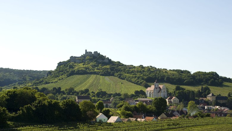 Burgruine Falkenstein, © Michael Himml Landschaft mit Burg auf einem Hügel, Weinberge und Dorf mit Kirche im Vordergrund.