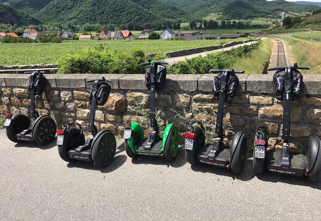 Auswahl an Segways, © Karoly Sechs Segways stehen vor einer Steinmauer mit Landschaft im Hintergrund.