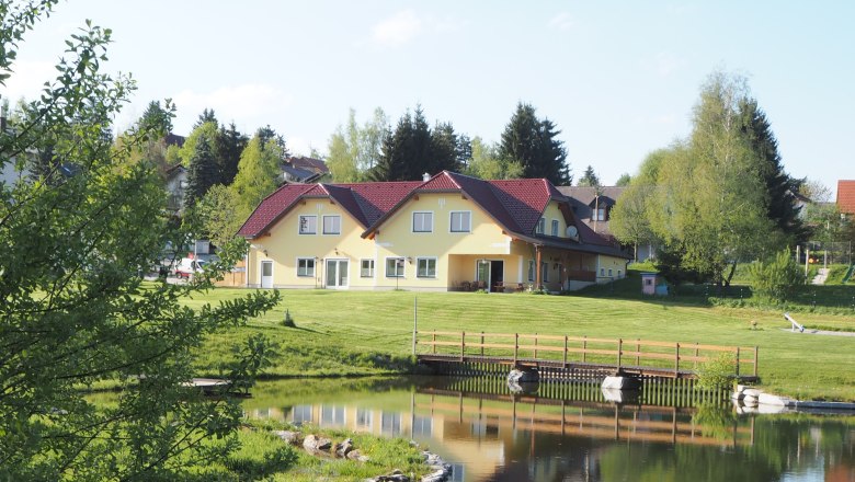 gesamte Anlage Freizeitzentrum, © MG Sallingberg Gelbes Gebäude mit rotem Dach an einem Teich, umgeben von Bäumen und Rasen.