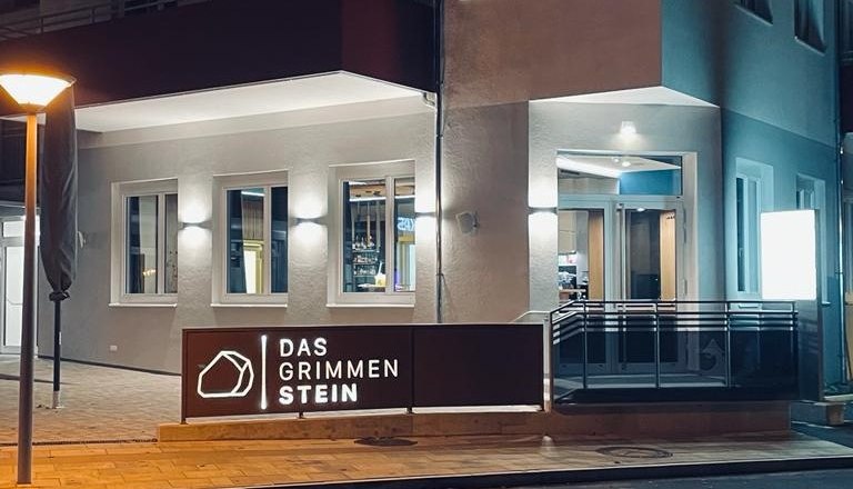 Das GrimmenStein außen, © Das GrimmenStein Außenansicht eines beleuchteten Gebäudes bei Nacht mit dem Schild 'Das GrimmenStein'.