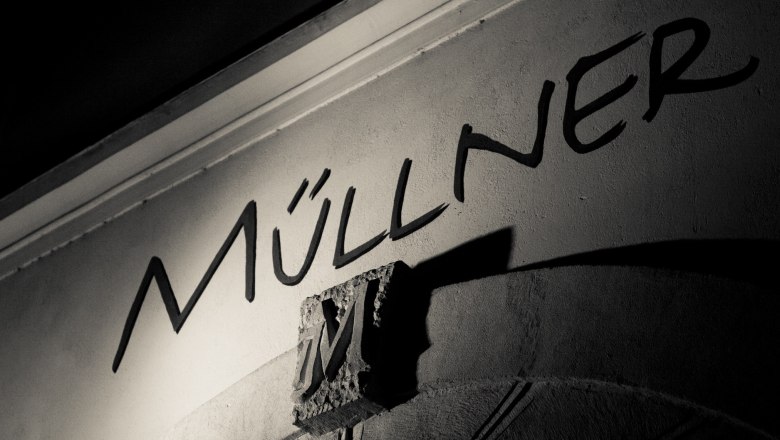 Logo, © Familie Müllner Schwarz-weißes Foto eines Schriftzugs 'Müllner' auf einer Wand mit einem dekorativen 'M'.