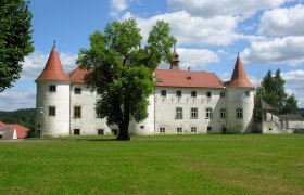 Gemeinde Dobersberg, © Gemeinde Dobersberg Ein historisches Schloss mit roten Dächern und Türmen, umgeben von grüner Wiese und Bäumen, unter einem blauen Himmel mit weißen Wolken.