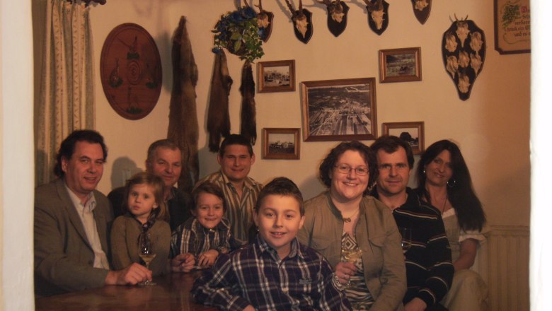 Familie Reinschedl, © Fam. Reinschedl Eine Gruppe von Menschen sitzt in einem Raum mit Jagdtrophäen an der Wand.